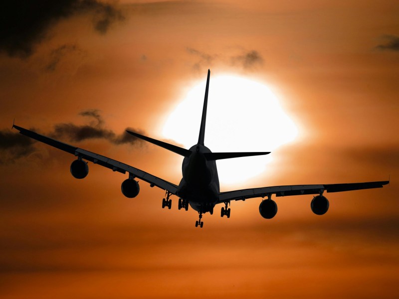 Image of an airplane flying toward the sun through a hazy sky.