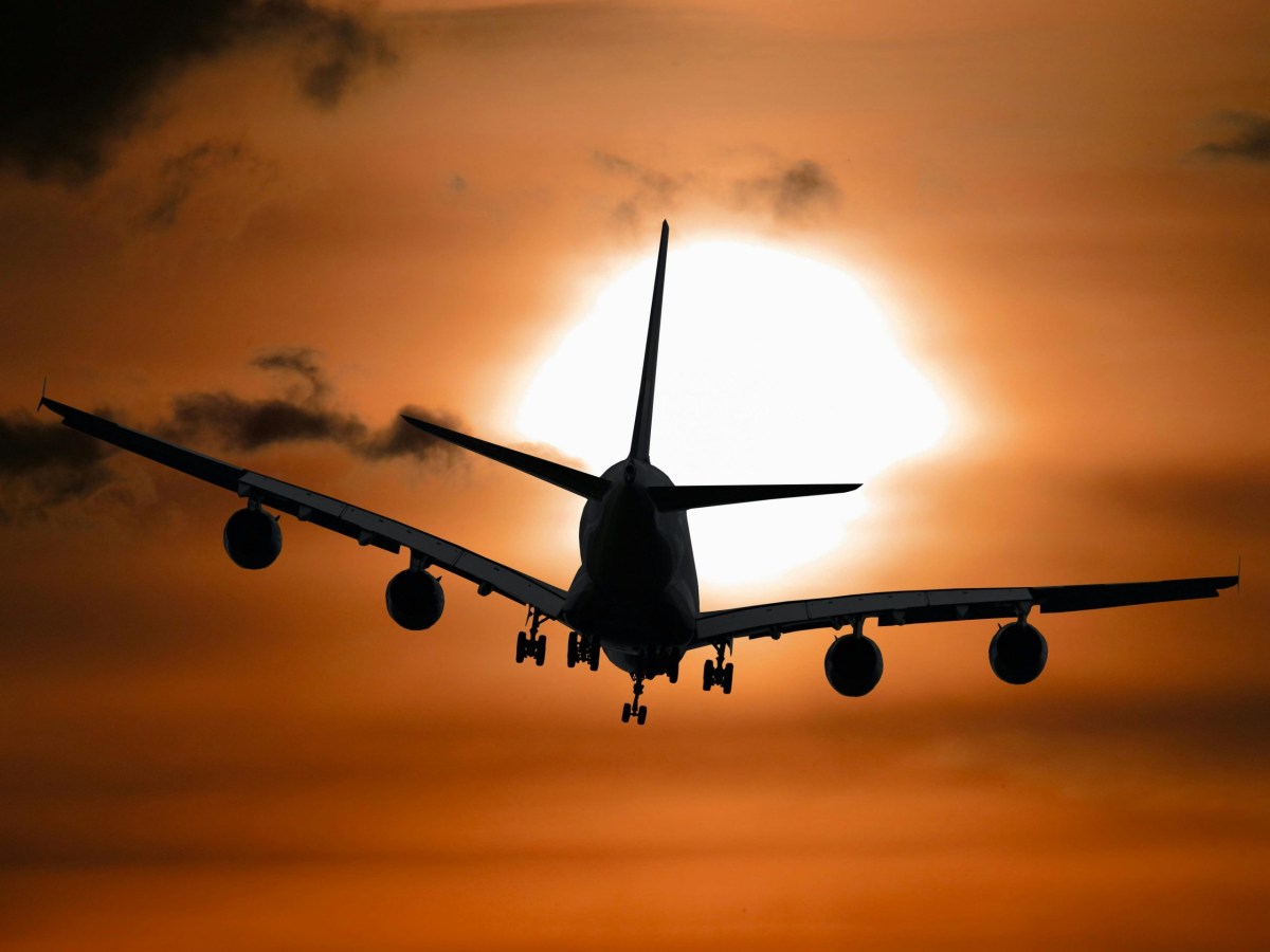 Image of an airplane flying toward the sun through a hazy sky.
